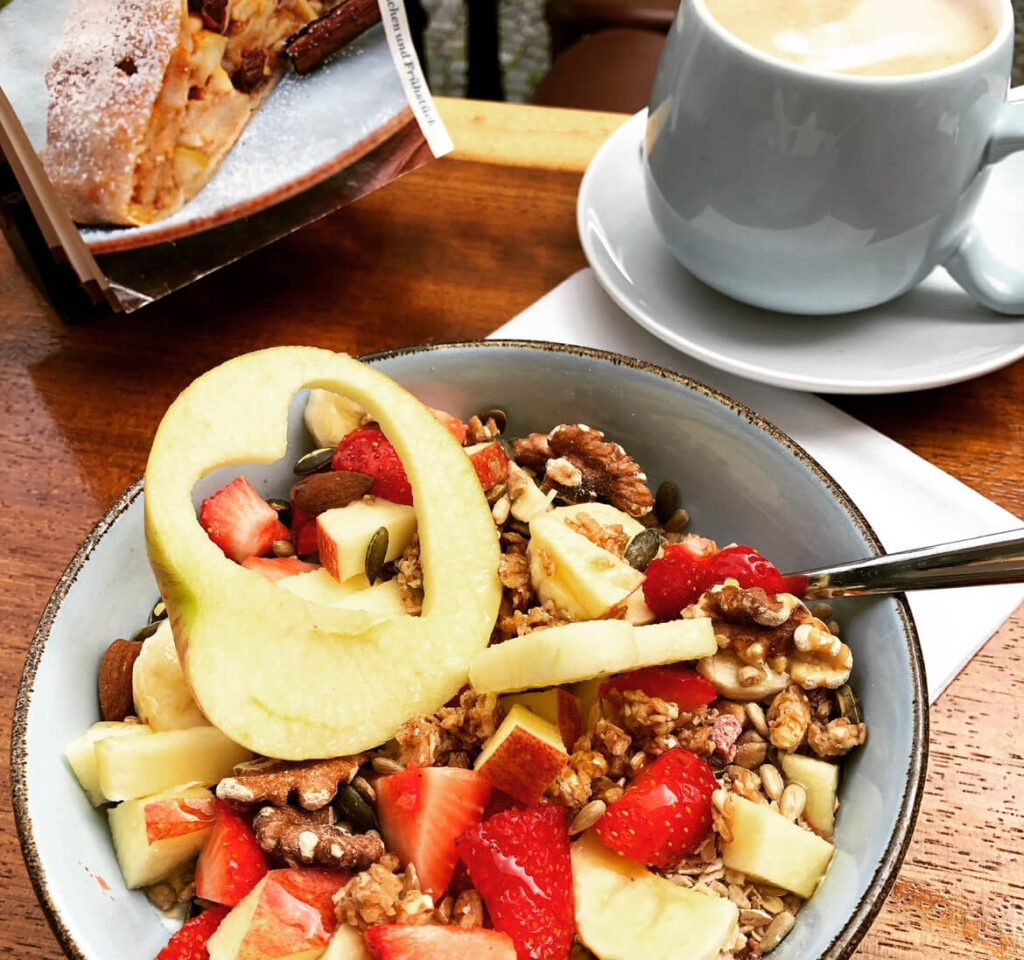 Köstliches Frühstück mit hausgemachtem Müsli, Granola und Milchkaffee draussen auf der Terrasse im inhabergeführten Kaffeein in Ulm